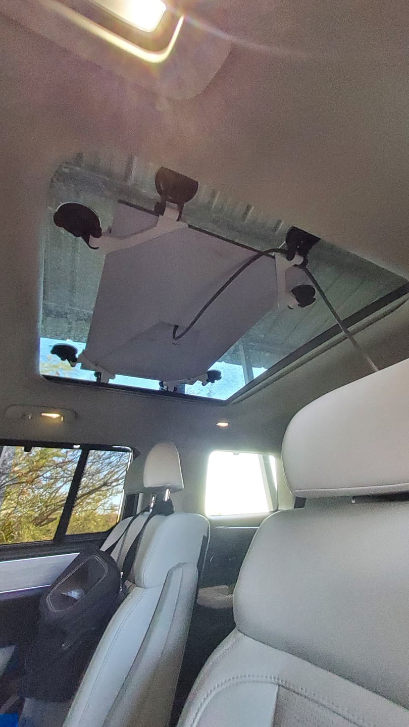 Starlink Gen 3 Standard 4 dish held flat against a panoramic sunroof from inside the cabin by locking suction cups, cable routed down